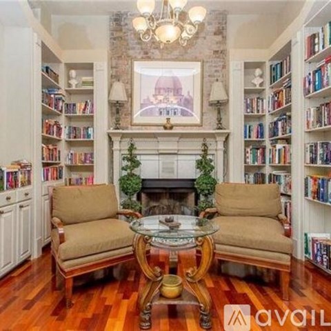 A living room with a fireplace, bookshelves, and a painting of a building.