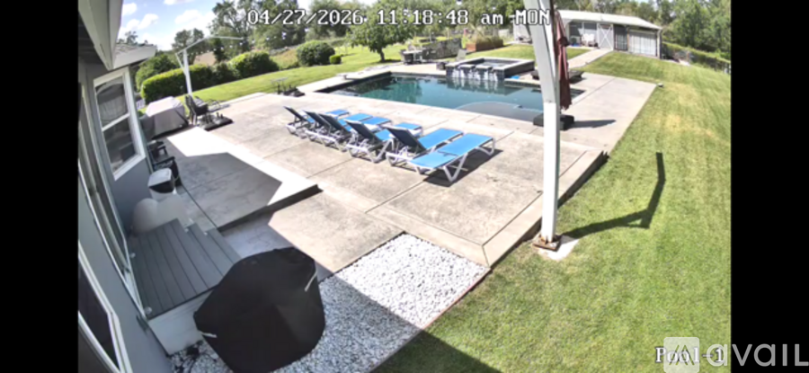 A pool with a few chairs and a table is visible from a house.