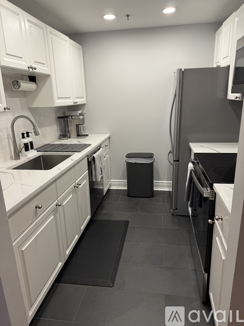 A kitchen with white cabinets and a black trash can.