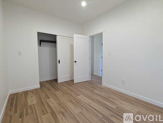 A room with a white wall and wooden flooring with a door and a closet.