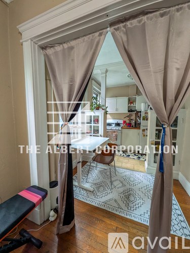A room with a view of a kitchen through a window with curtains.