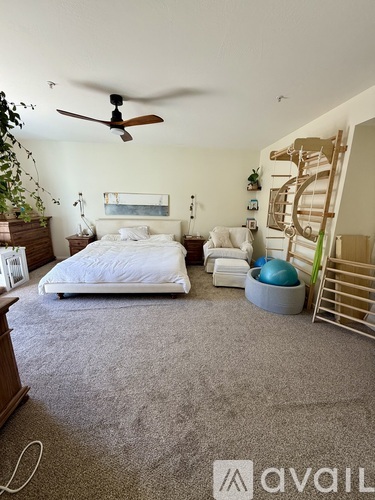 A bedroom with a bed, a fan, and a staircase.