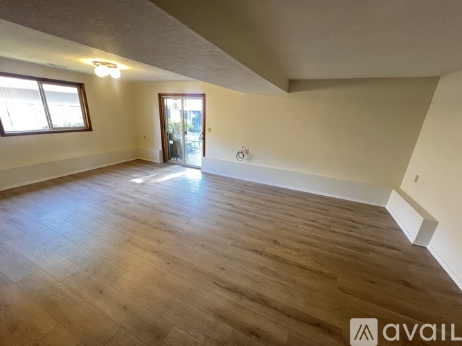 A spacious room with wooden flooring and a door leading to another room.