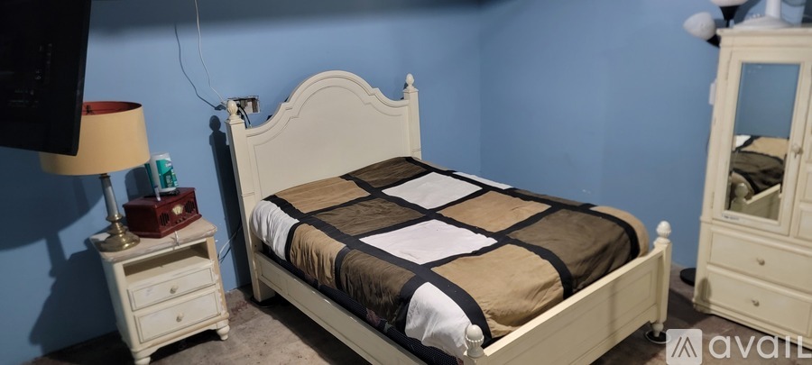 A white bed with a brown comforter and a white nightstand with a lamp on it.