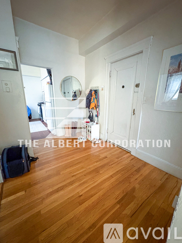 A room with wooden floors and white walls, with a mirror and a door visible.