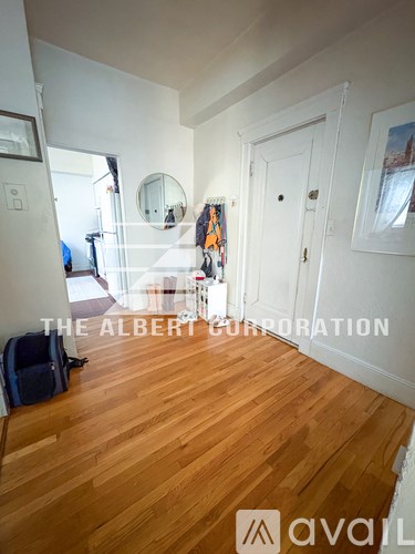 A room with wooden floors and white walls, with a mirror and a door visible.