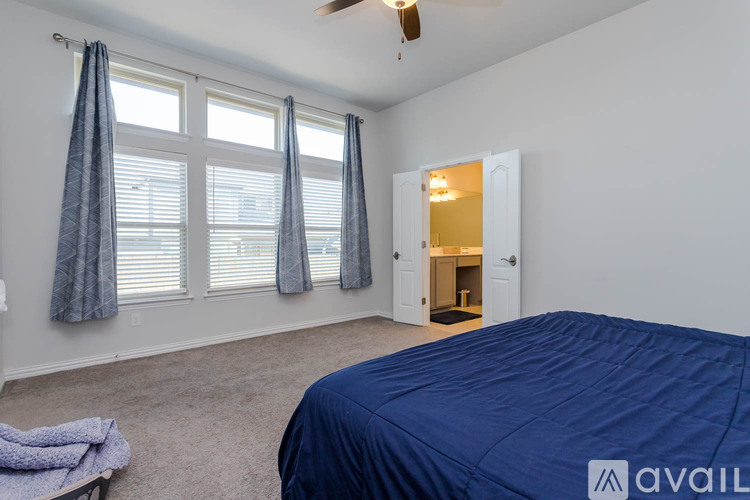 A bedroom with a bed covered in a blue sheet and a ceiling fan.