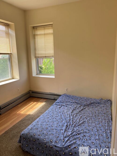 A bedroom with a bed covered in a blue comforter and two windows with blinds.
