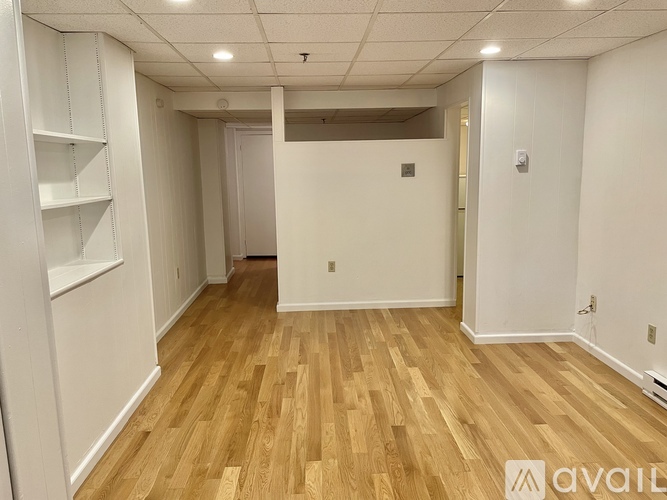 A room with wooden flooring and white walls, with a doorway leading to another room.