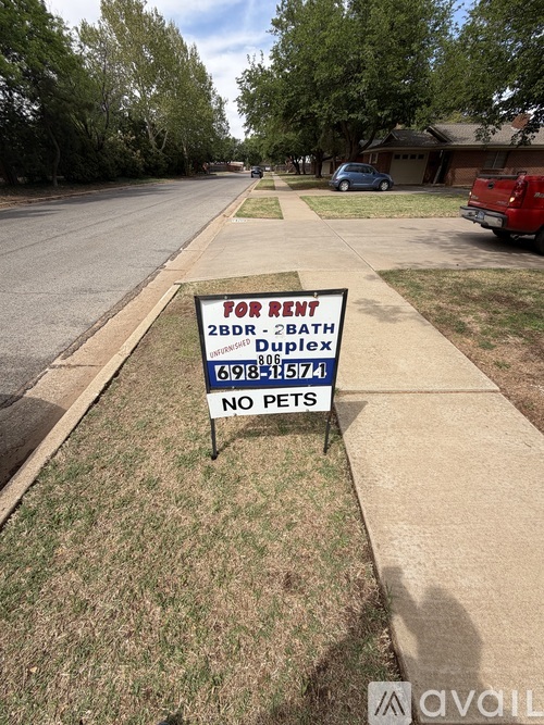 A for rent sign is on the grass by the road.