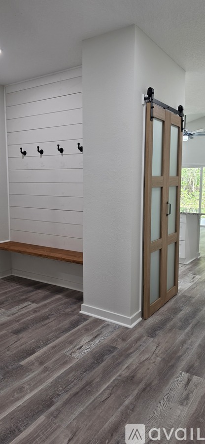 A room with a wooden floor and a white wall with a row of hooks on it.