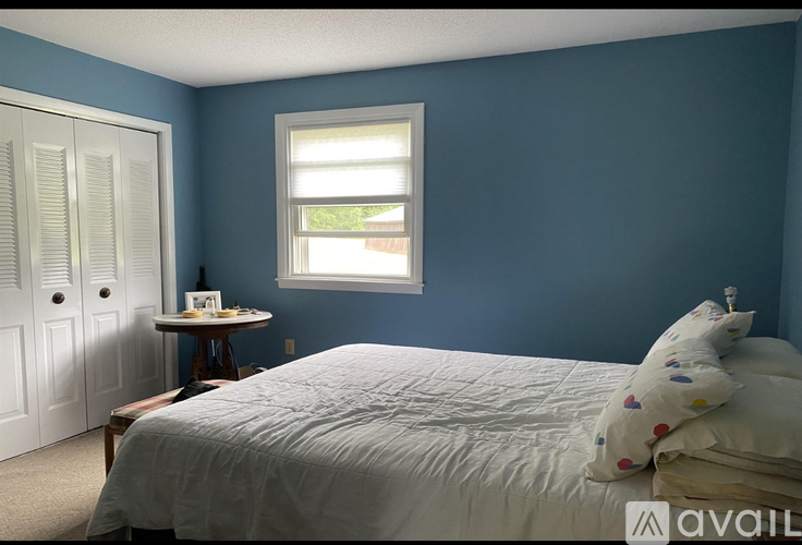 A bedroom with a bed, a small table with a lamp, and a window.