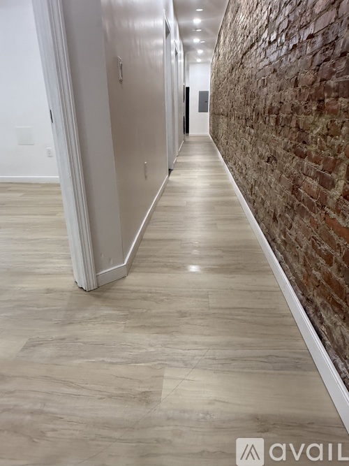 A long hallway with a brick wall on one side and a wooden floor.