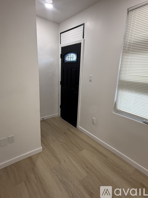 A black door with a glass window is in a room with white walls and wooden flooring.