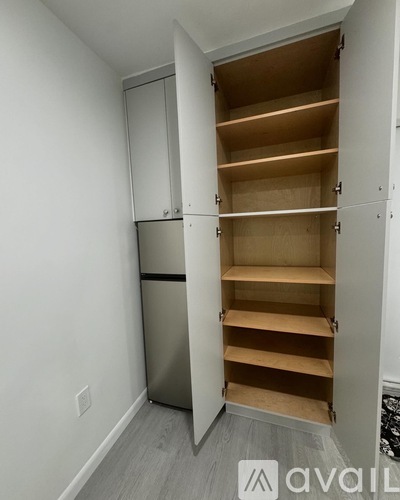 A kitchen pantry with a white wall and a silver refrigerator.