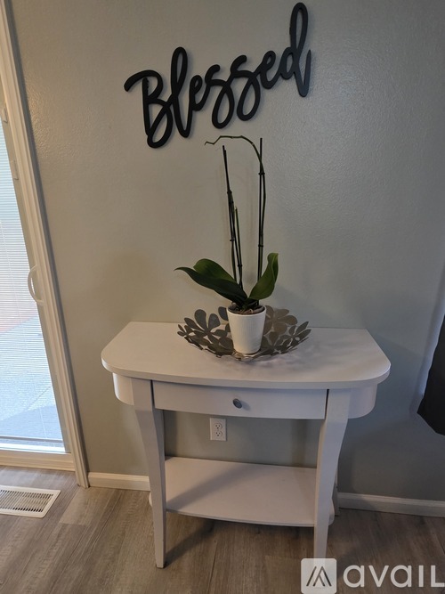 A small table with a potted plant on it and a wall decal that says "Blessed".