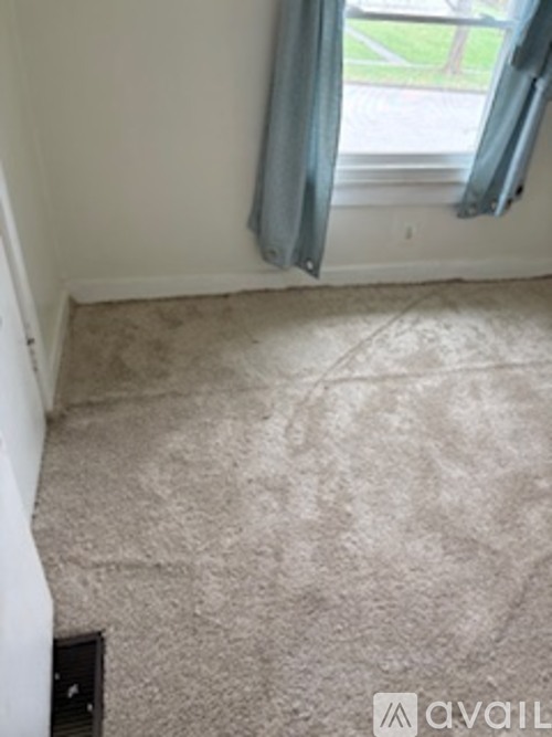 A room with a carpeted floor and a window with a view of a lawn outside.