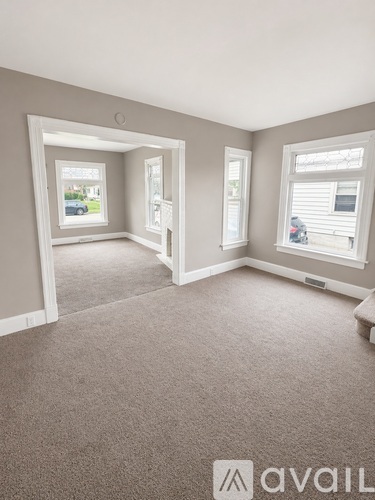 A carpeted room with a window and a door leading to another room.