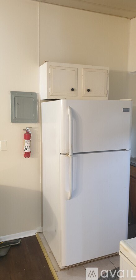 A white refrigerator in a kitchen with a grey electrical outlet and a fire extinguisher on the wall.