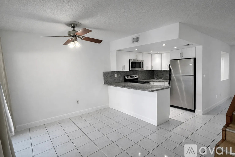 A kitchen with a refrigerator, microwave, and a fan.