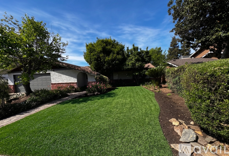 A well-maintained lawn leads to a house with a stone path and bordered by trees and shrubs.