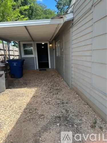 A gravel covered backyard with a blue trash can and a white house.
