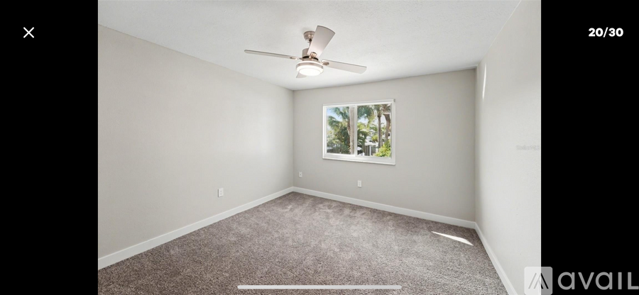 A room with a ceiling fan and a window showing trees outside.