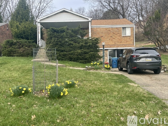 A house with a car parked in front and a fence with yellow flowers.