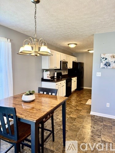 A kitchen with a table and chairs in the foreground and a refrigerator, microwave, and oven in the background.