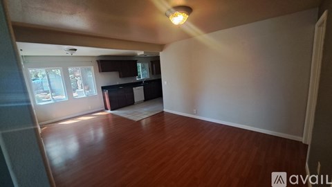 A room with wooden floors and a kitchen area in the background.