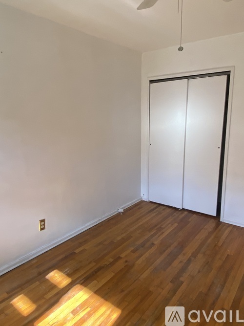 A room with a wooden floor and a white wall with a hanging fan.