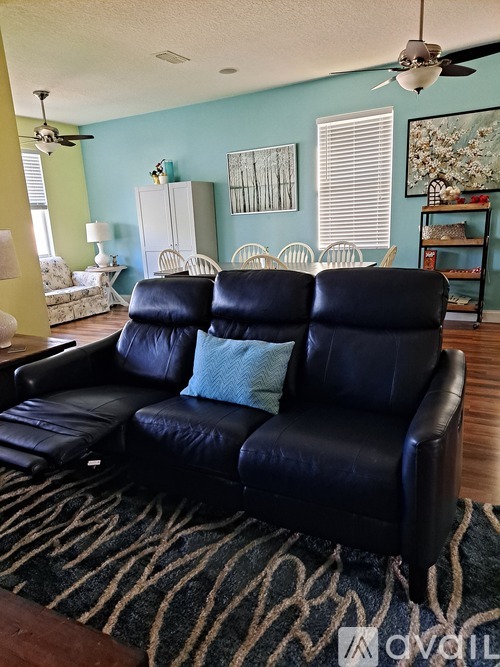 A black leather sofa with a blue pillow sits in a room with a ceiling fan.