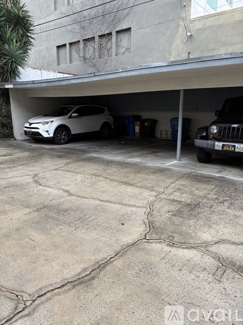 A white car is parked in a garage under a concrete building.