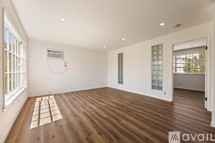 A spacious room with wooden flooring and a window on the left side.