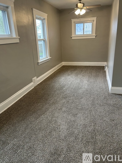 A room with grey carpet and two windows.