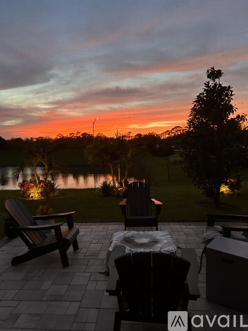 A patio with a table, chairs, and a view of a lake at sunset.