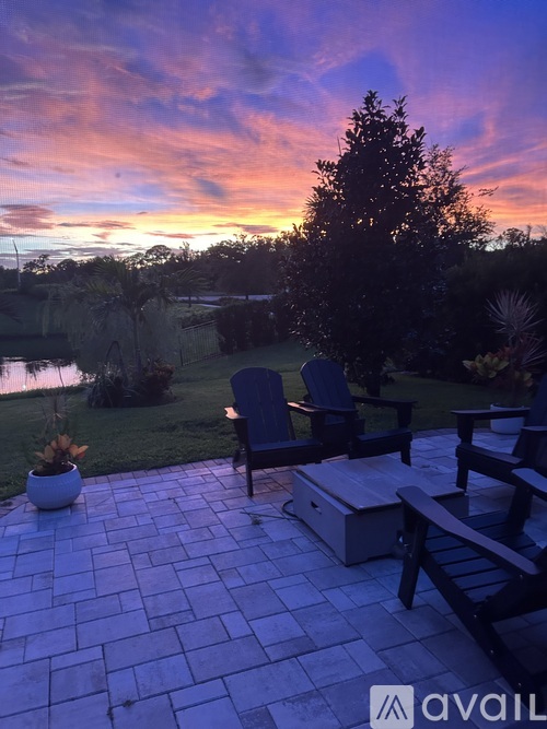 A patio with a table and chairs overlooking a body of water at sunset.