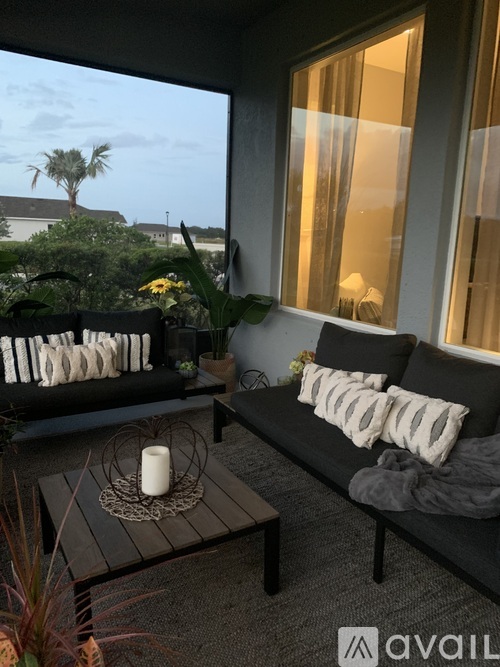A patio with a couch, table, and candle on a table with a view of the outside.
