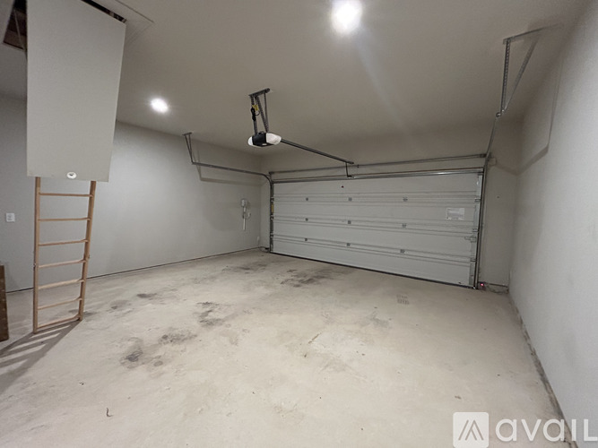A large, empty garage with a closed white door and a ladder on the left side.