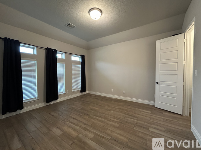 A room with a white door, black curtains, and wooden flooring.