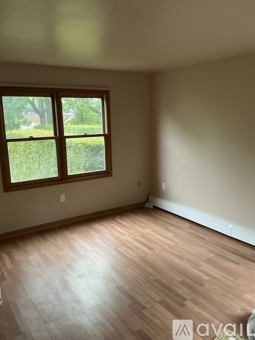 A room with wooden flooring and a window overlooking a green lawn.