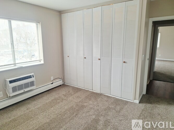 A room with a window, a wall-mounted air conditioner, and a row of white closets.
