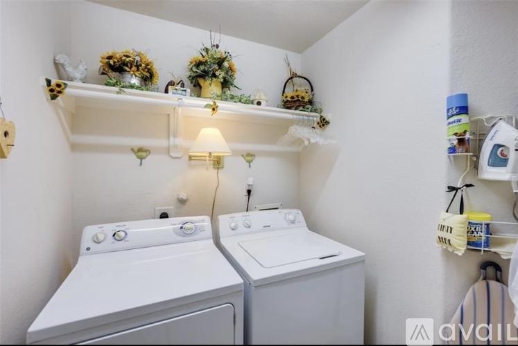 A laundry room with two washing machines and shelves with decorations and a lamp.