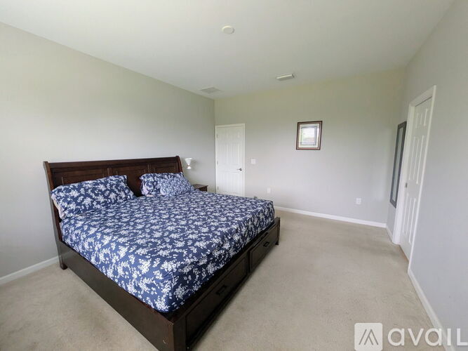 A bedroom with a bed, carpeted floor, and a picture on the wall.