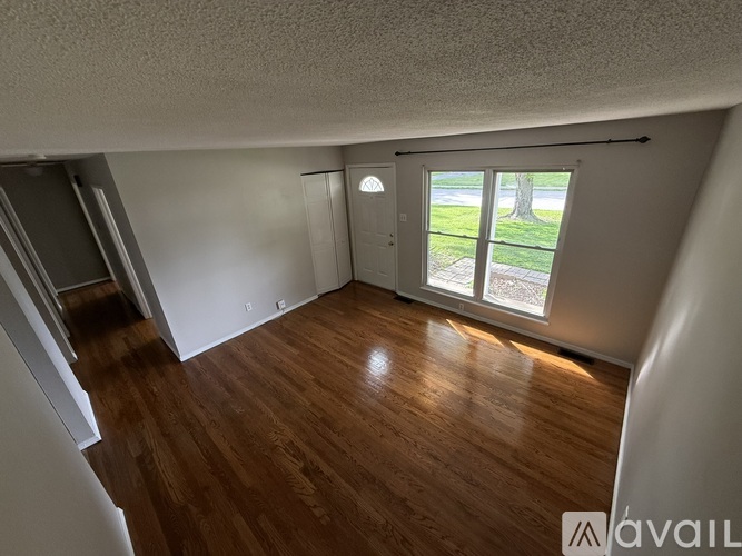 A room with wooden floors and a window overlooking a lawn.