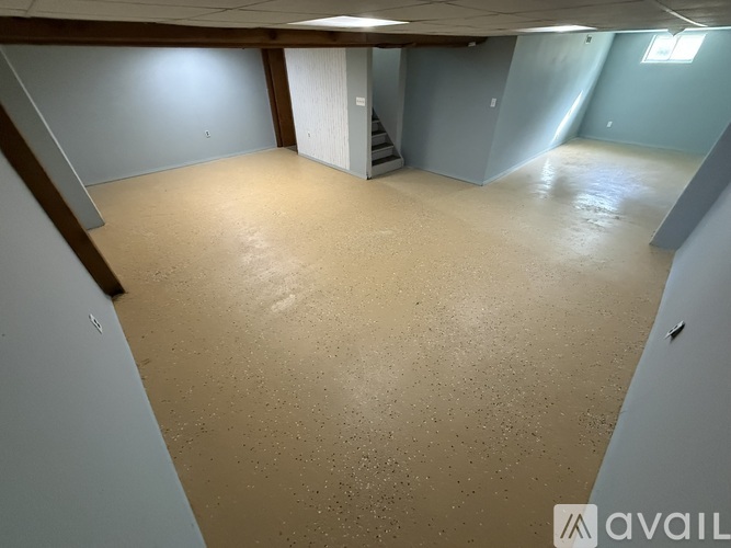 A spacious room with a carpeted floor and a staircase in the background.