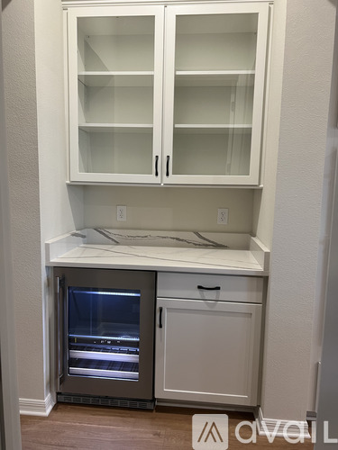 A white kitchen cabinet with glass doors and a drawer is open.