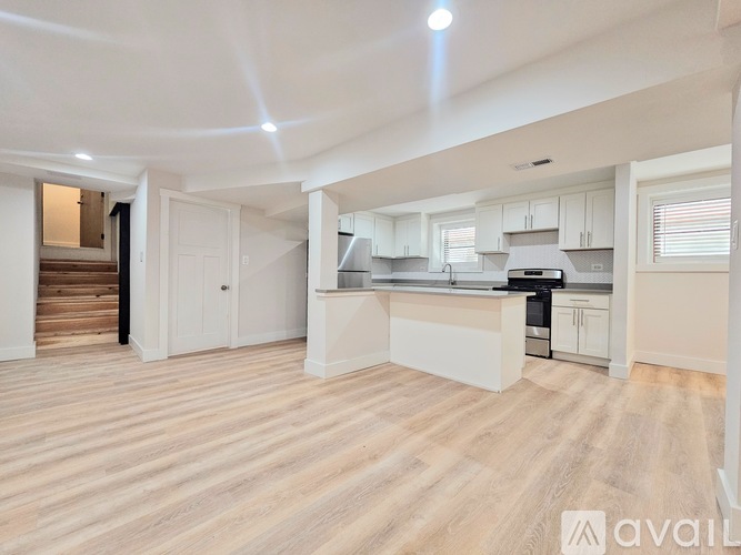 A spacious kitchen and living area with wooden flooring and white cabinetry.