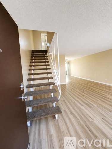 A staircase with a carpeted runner and wooden steps leads to a bright room.