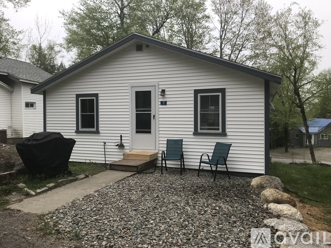A small white house with a black grill and two chairs.